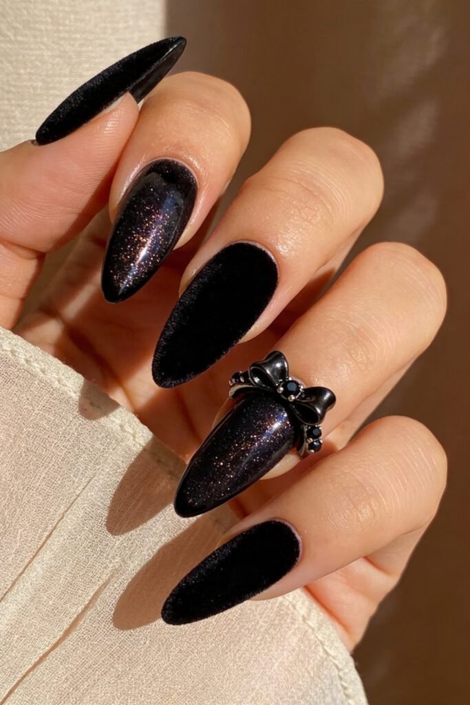 Black Valentines Day Nails That Feel Chic And Romantic 17 Long almond-shaped black valentines day nails with a mix of velvet and glitter finishes, paired with a matte black bow ring to enhance the luxurious feel.