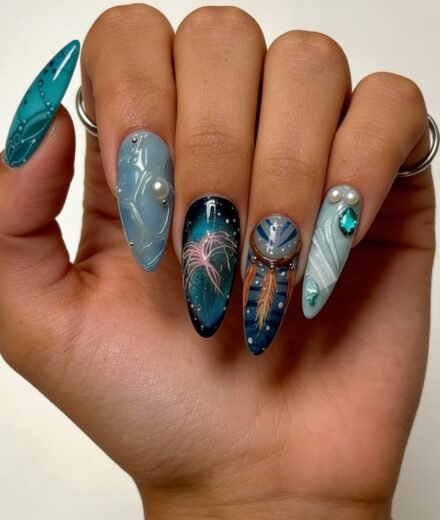 Hand with long almond-shaped nails featuring an oceanic theme in blue and teal tones, with detailed feather and jellyfish-like designs, pearls, gemstones, and fine line art, evoking a mystical, avatar nails aesthetic.