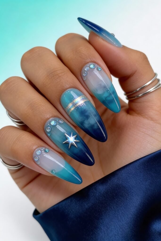Set of coffin-shaped avatar nails in ombre blue shades with sparkly rhinestone clusters, a metallic stripe, and a 3D star charm, blending ethereal and aquatic elements.