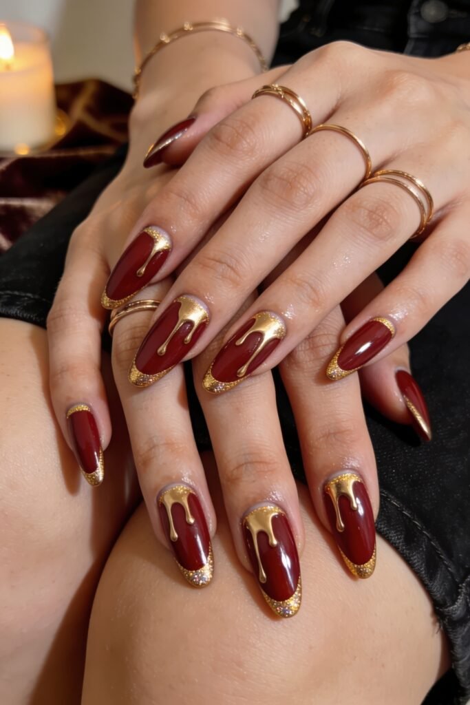 Fire Nails That Look Expensive and Feel Effortless 2 Deep burgundy almond nails with gold drip accents and glittery gold French tips, hands stacked together
