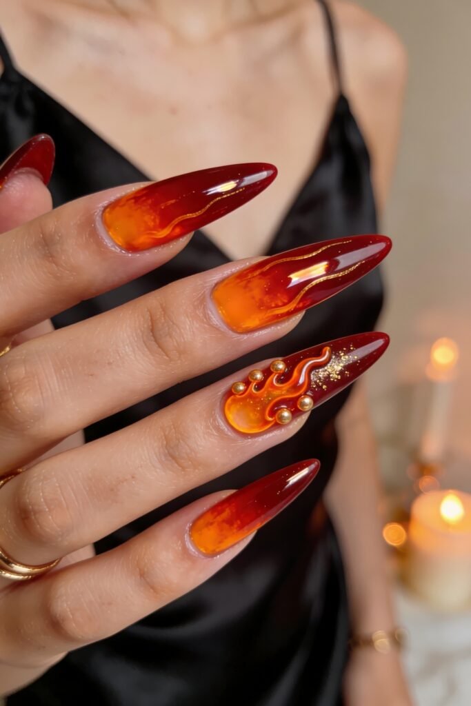 Fire Nails That Look Expensive and Feel Effortless 22 Red stiletto Fire Nails with translucent amber bases, thin gold wave lines, and a 3D flame-and-stud accent nail