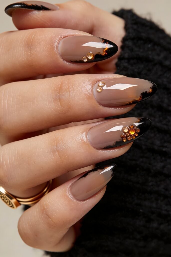 Fire Nails That Look Expensive and Feel Effortless 24 Close-up of nude almond nails with black smoky tips and gold rhinestone accents on a glossy finish