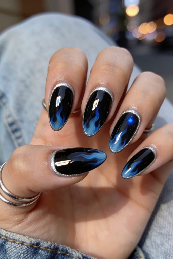 Fire Nails That Look Expensive and Feel Effortless 27 Glossy black almond Fire Nails with blue flame art and a silver glitter outline, hand on denim