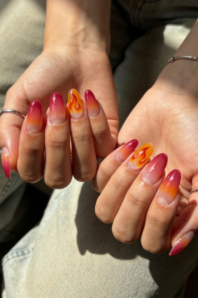 Fire Nails That Look Expensive and Feel Effortless 4 Two hands showing ombré pink-to-orange almond Fire Nails with flame decals on accent nails