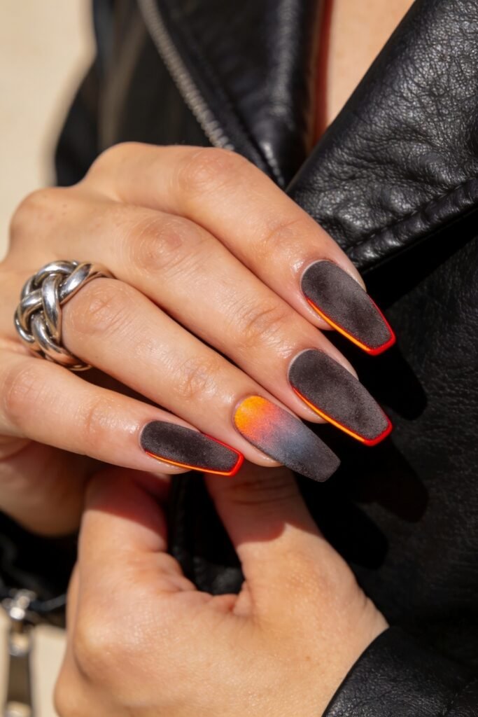 Fire Nails That Look Expensive and Feel Effortless 6 Matte charcoal coffin nails with neon red outline and a smoky orange gradient accent, hand in leather jacket