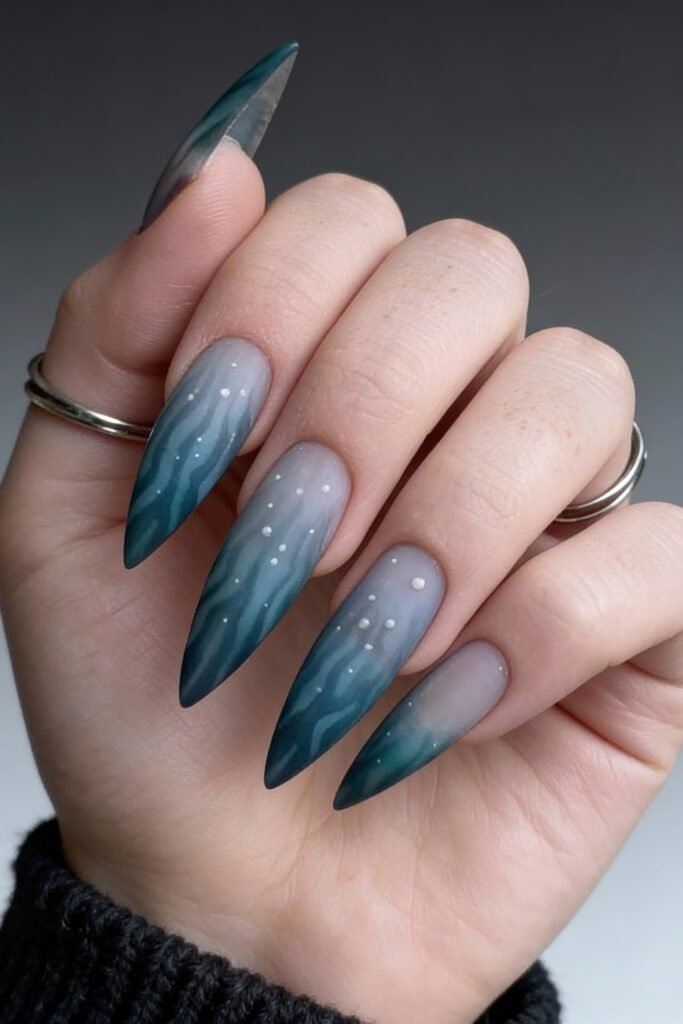 Long stiletto nails with a deep teal to gray gradient, featuring soft wave-like lines and scattered white dots, evoking an underwater or bioluminescent ocean effect.