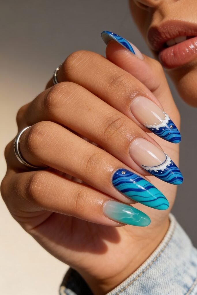 Artistic ocean wave nails with bright blue and turquoise hues, layered lines to mimic wave movement, foamy accents, and one translucent teal nail for added texture.