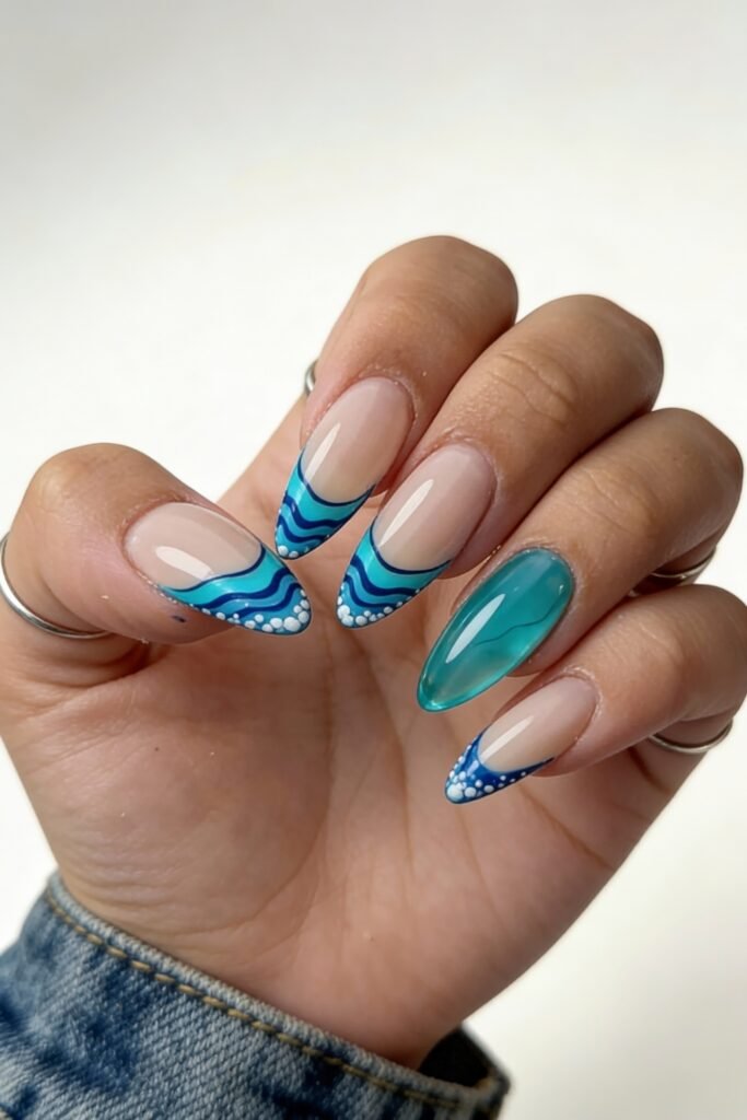 Vivid avatar nails with abstract blue wave French tips and dotted edges on a nude base, paired with a glossy, jelly-textured teal accent nail for a playful water-themed look.