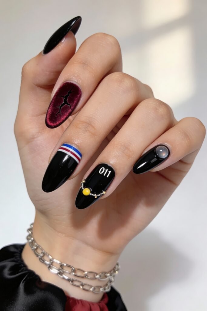 Glossy black and burgundy nails with Stranger Things elements including a red crack design, “011” text with a yellow charm, a blue-white-red stripe, and a cloudy glass bead accent.