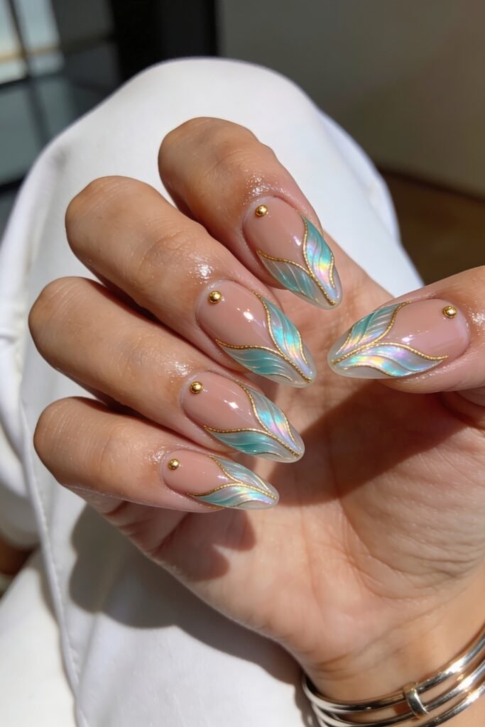 Close-up of iridescent teal leaf French tips outlined in gold on nude nails with tiny gold studs and rings