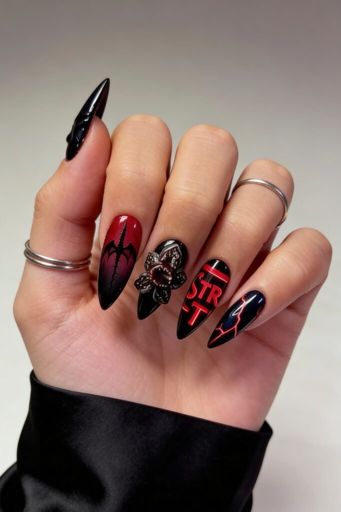 A Stranger Things nail set with stiletto tips, showcasing a black Demogorgon silhouette, 3D flower centerpiece, neon-style red “STR” text, and jagged lightning bolts on a black base.