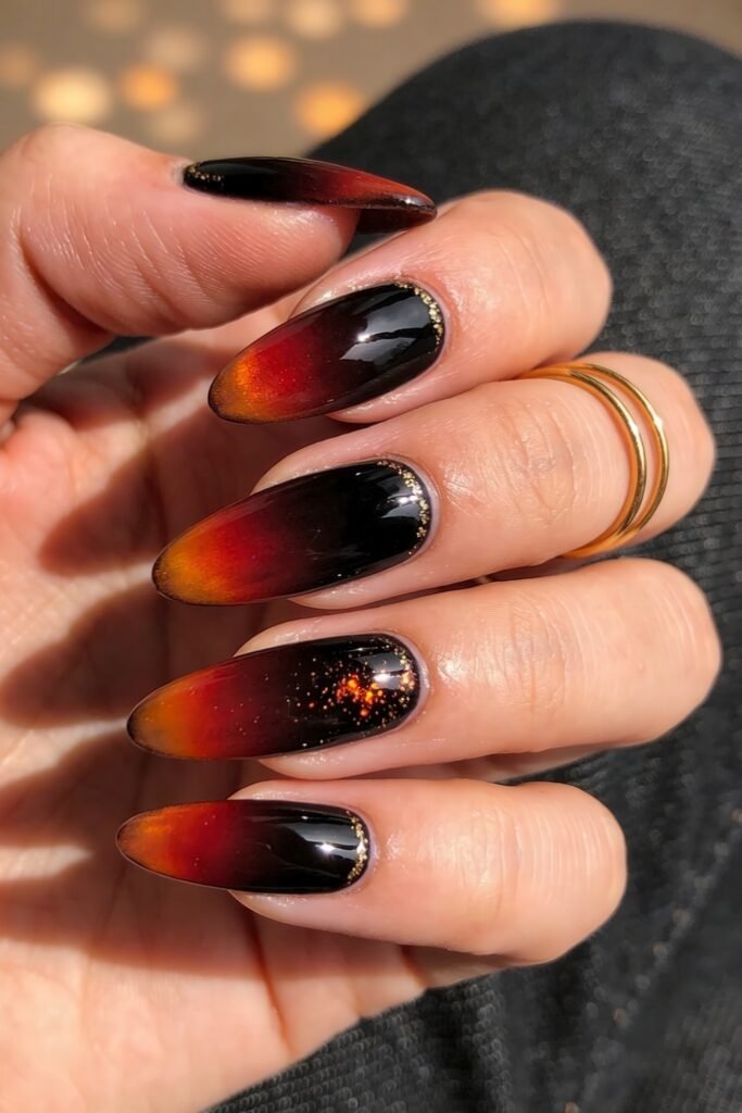 Fire Nails That Look Expensive and Feel Effortless 14 Glossy almond Fire Nails in black-to-red ombré with amber tips and scattered gold glitter accents