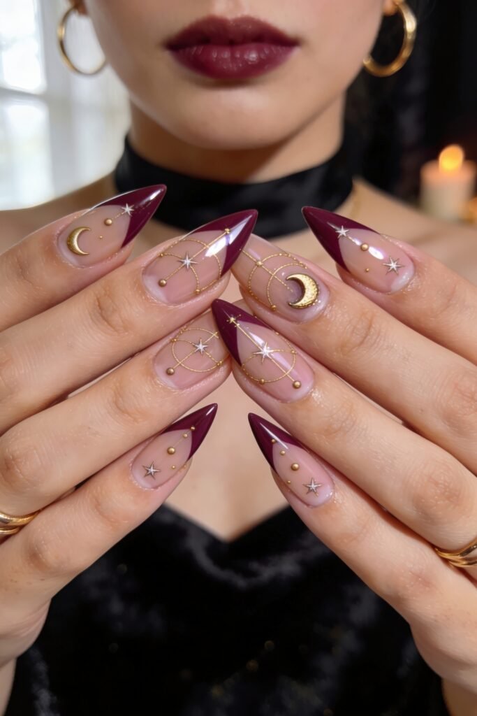 Both hands showcasing matching celestial Goddess Nails on stiletto shapes with sheer bases, dark burgundy chevron tips, and intricate gold star and moon patterns