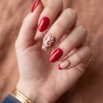 Chic Gold and Red Nails for a Bold, Polished Look Hand with glossy red almond nails featuring leopard print accent nails and a red French tip against a warm blurred background
