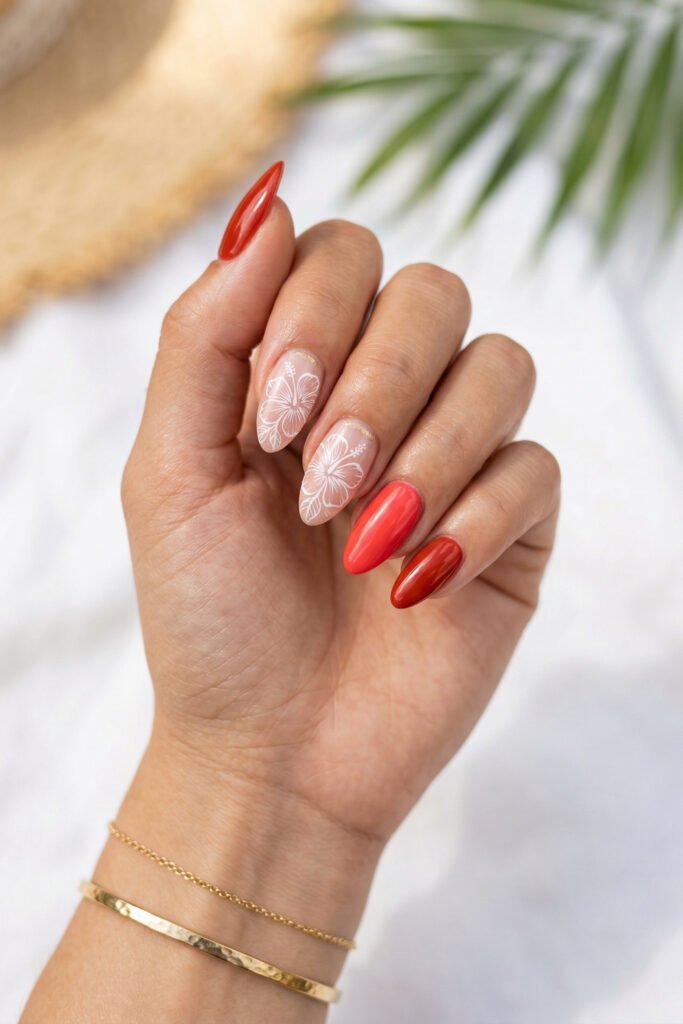 Close up of almond nails with white hibiscus art on nude polish and glossy coral red accents against a soft tropical background