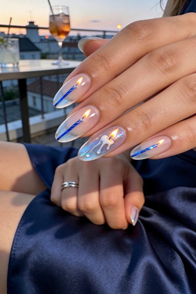 Hand resting on a satin dress at sunset, showing long sheer nails with blue candle and dripping wax nail art that looks like tiny lit candles