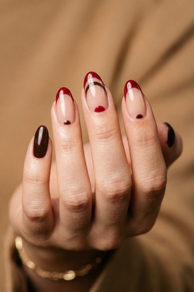 Brown And Red Nails That Make Every Look Richer 2 Hand showing almond nails with red French tips brown curved accents and dark brown polish against a warm beige background