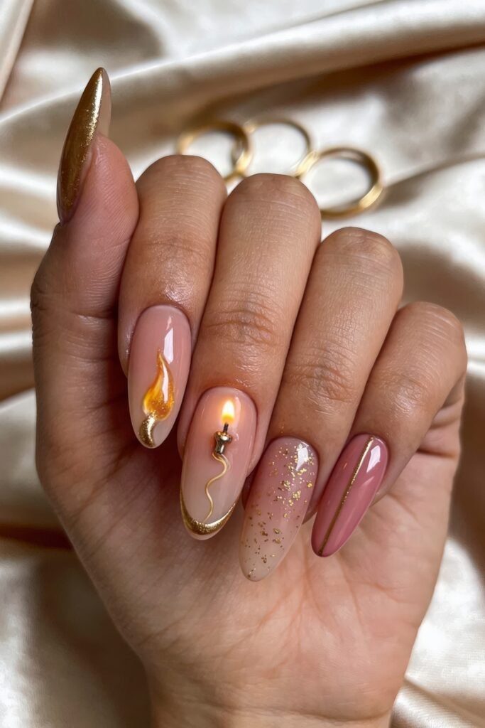 Gold Birthday Nails That Feel So Chic 2 Close-up of glossy almond nails in sheer pink and mauve with gold accents, including a flame design, a candle motif, gold glitter, and a metallic stripe on one nail