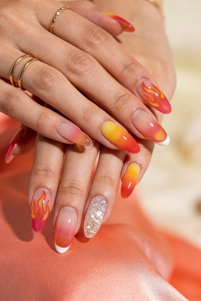 Summer Birthday Nails That Feel Fresh and Fun 2 Two hands with almond nails featuring orange and yellow ombre designs with flame art white tips and one silver glitter accent nail