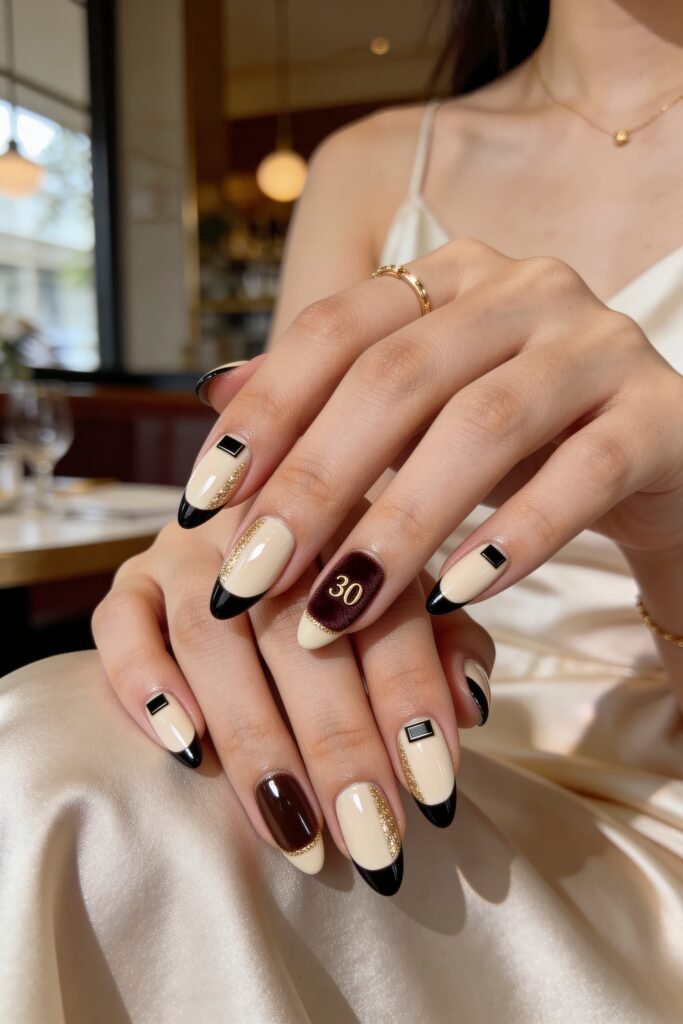 Two hands with cream almond nails featuring black French tips, gold glitter lines, black square accents, and a burgundy textured accent nail