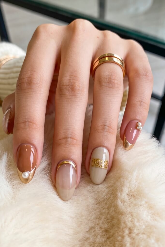 Gold Birthday Nails That Feel So Chic 19 Close-up of almond nails in nude, beige, and pink with gold French tips, pearl accents, and a date detail reading 09.28