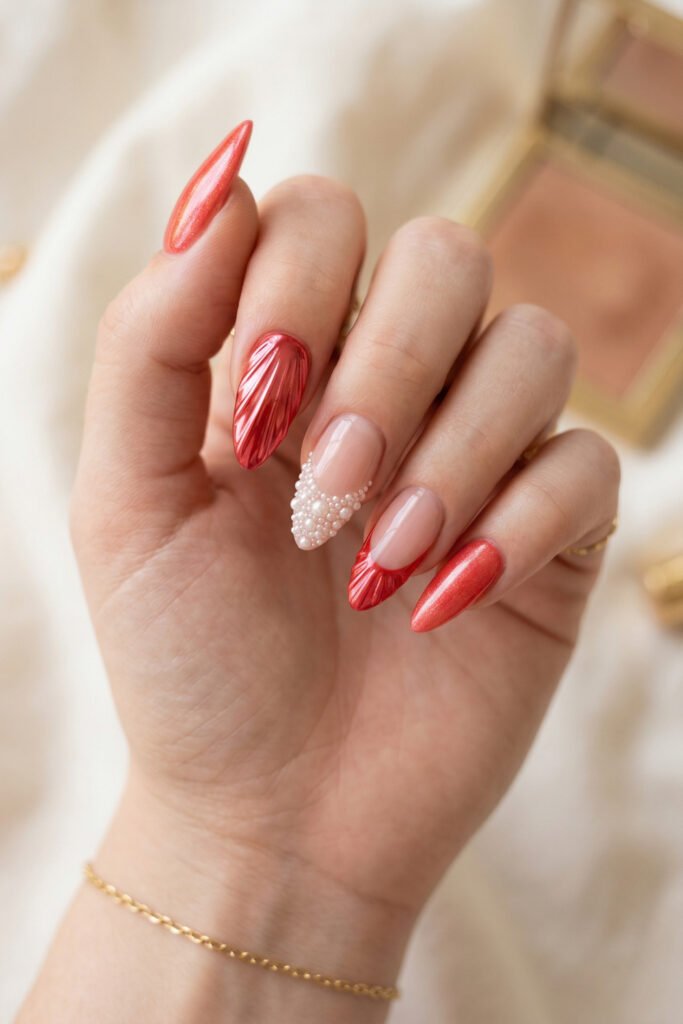 Close up of almond nails with coral chrome shell details a pearl covered accent nail and a soft red French tip design