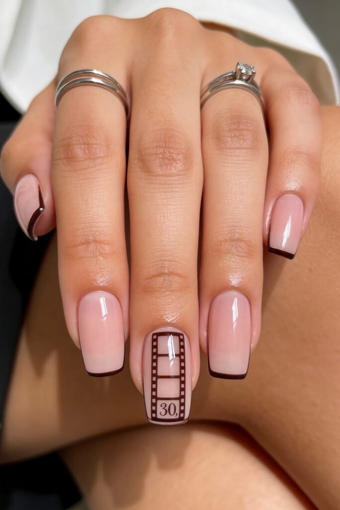 Close-up of pale pink square nails with thin burgundy French tips and a filmstrip accent nail