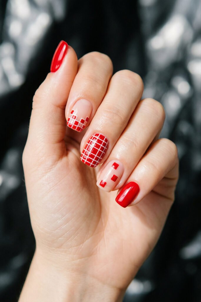 Short square nails with glossy red polish white grid nail art and minimalist red square accents against a dark background