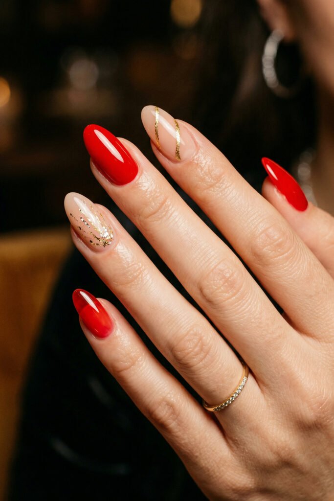 Almond nails with glossy red polish and nude accent nails featuring fine gold lines and sparkling gold foil in warm evening light