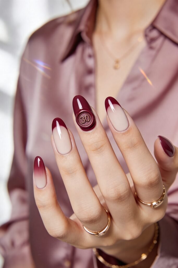 Close-up of nude almond nails with deep burgundy French tips and a raised wax-seal accent nail