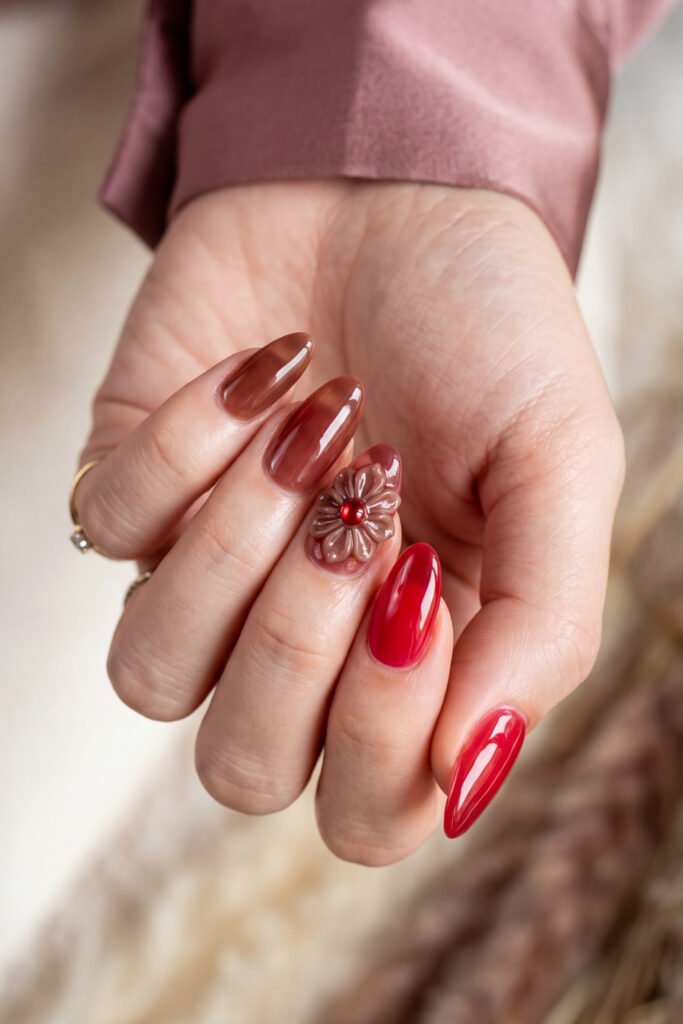Brown And Red Nails That Make Every Look Richer 24 Hand with glossy taupe and bright red almond nails featuring a 3D flower accent with a red jewel center