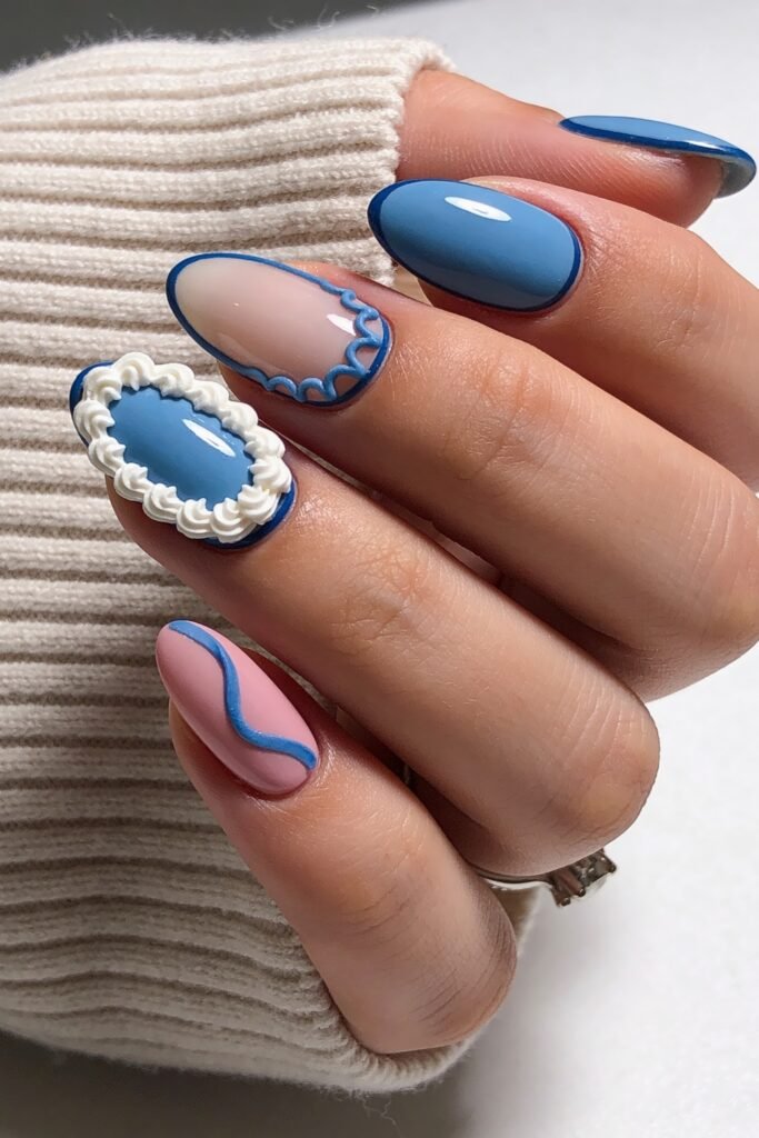 Close-up of almond-shaped nails in soft blue, pink, and white with raised frosting-like 3D details, framed by a cream sweater sleeve