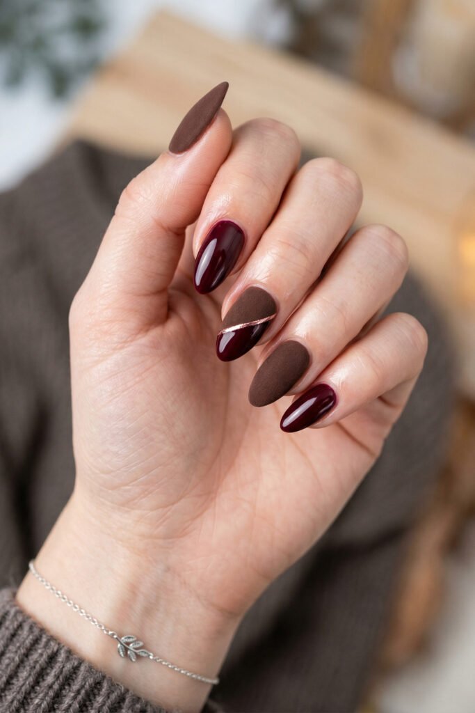 Brown And Red Nails That Make Every Look Richer 4 Hand with glossy burgundy and matte brown almond nails featuring a rose gold diagonal accent against a cozy neutral background