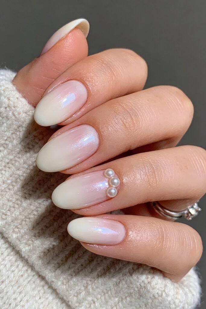 Close-up of soft pink to milky white ombré almond nails with an iridescent sheen and a small pearl cluster accent