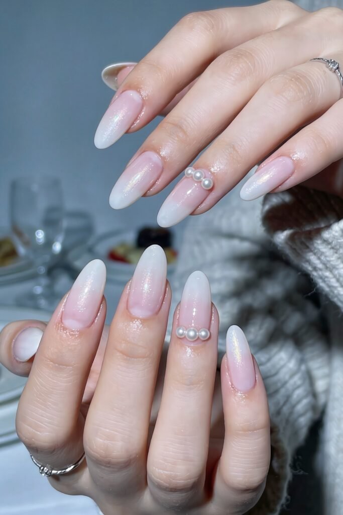 Two hands with glossy pink to white ombré almond nails with an iridescent finish and pearl cluster accents