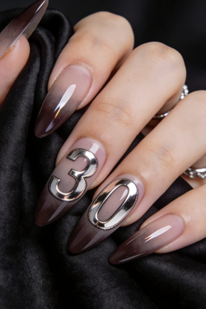 Close-up of smoky taupe ombré stiletto nails with large silver chrome number accents on two nails, holding black satin fabric
