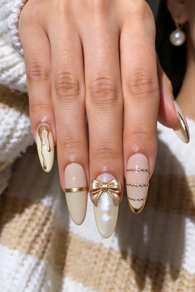 Gold Birthday Nails That Feel So Chic 8 Close-up of ivory and blush almond nails with gold details including a metallic drip design, a gold band, a pearly nail with a 3D gold bow, and a stitched accent nail