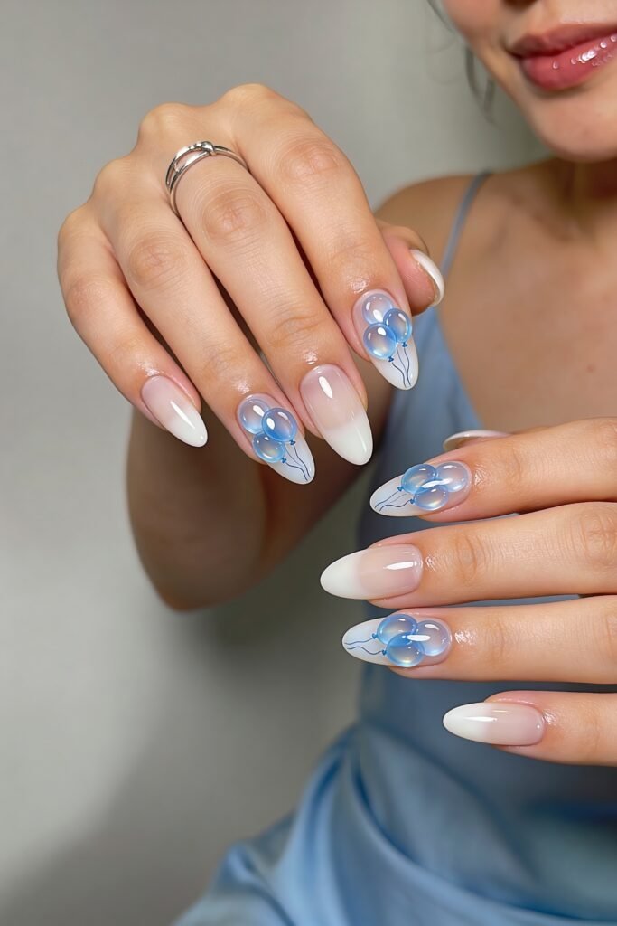 Person in a light blue dress showing almond-shaped ombré white nails with translucent blue balloon nail art on several fingers
