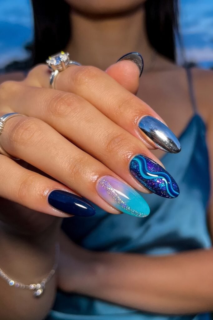 Summer Birthday Nails That Feel Fresh and Fun 9 Hand with almond nails featuring deep navy chrome glitter and blue lavender ombre designs with a wavy accent against a blue satin outfit