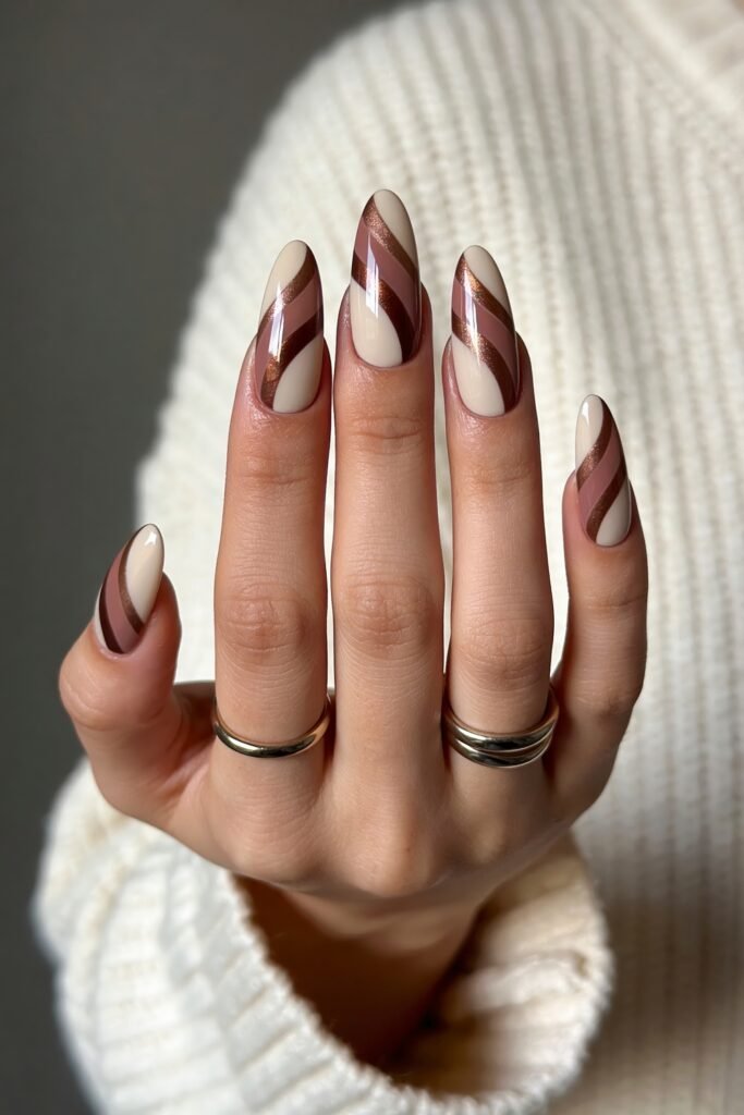 Close-up of almond nails with a creamy ivory base and flowing brown, mauve, and bronze swirl designs, framed by a chunky knit sleeve