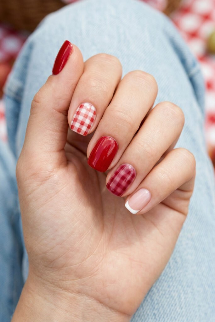 Short square nails with glossy red polish red gingham accents and a white French tip styled over light blue denim