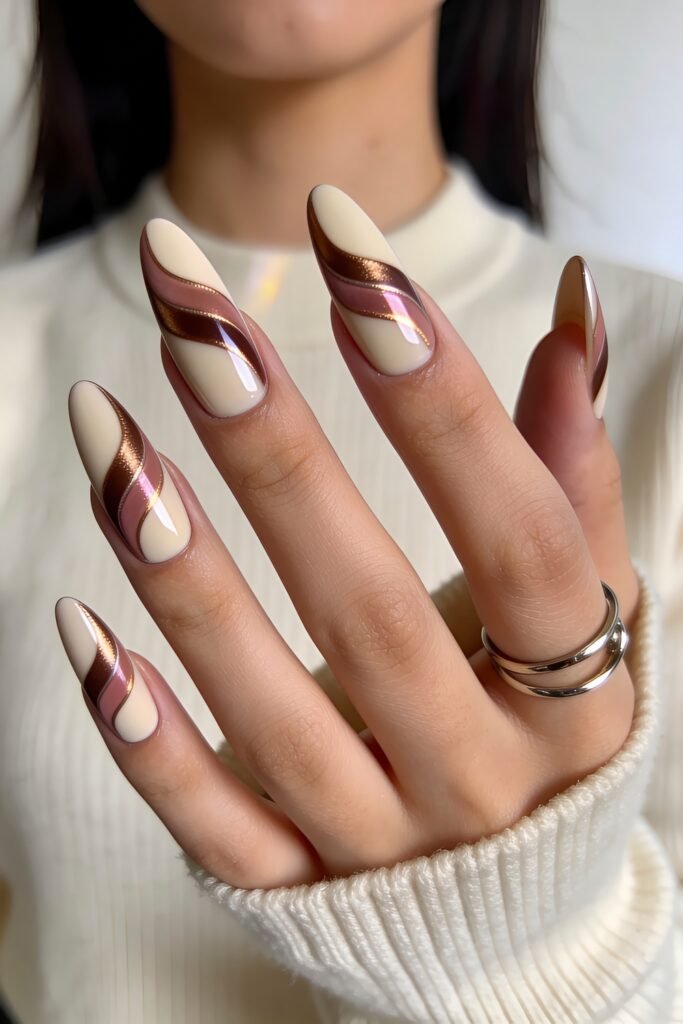 Close-up of almond nails with a creamy ivory base and pink, brown, and metallic bronze wavy stripe nail art