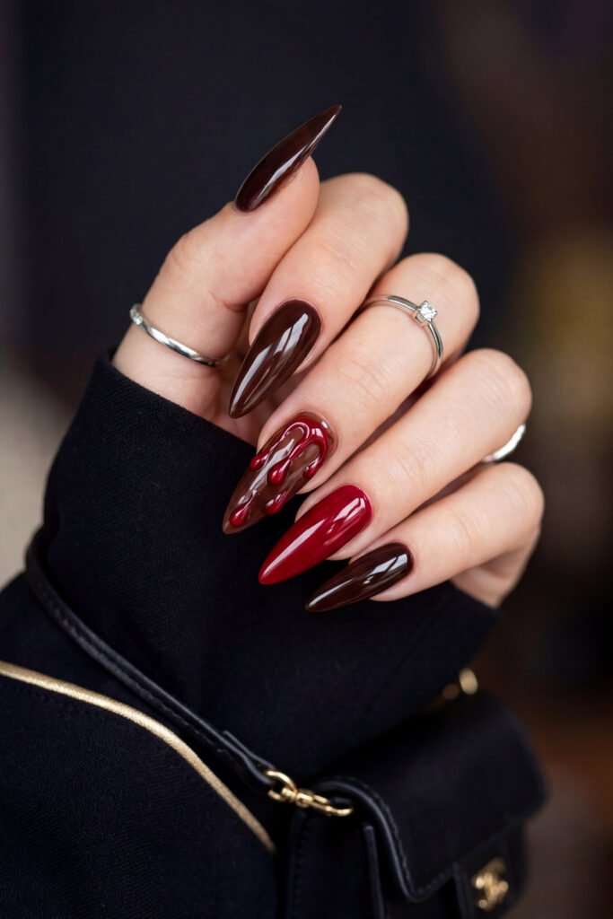 Brown And Red Nails That Make Every Look Richer 13 Close up of glossy brown and red stiletto nails featuring a red dripping accent design against a dark blurred background