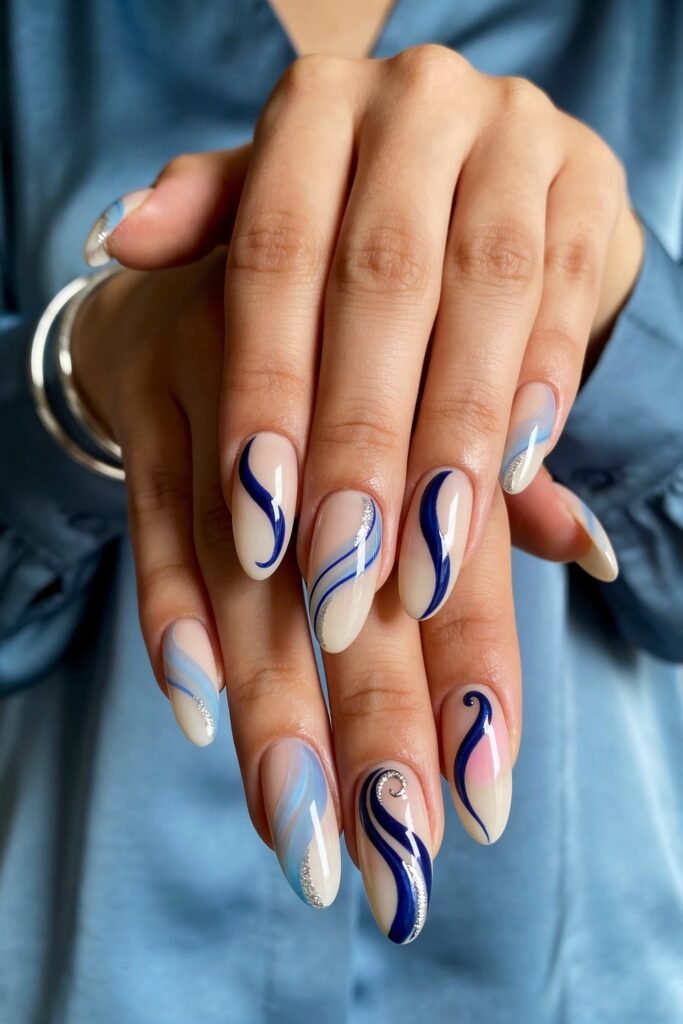 Close-up of long almond nails with flowing blue and white swirl designs, soft nude and pink gradients, and silver glitter accents