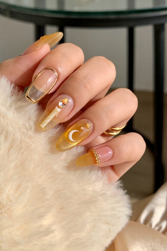 Gold Birthday Nails That Feel So Chic 15 Close-up of almond nails in nude and amber tones with gold detailing, featuring a clear gold-outlined tip, a candle motif with a gem flame, a crescent moon accent, and a rhinestone band