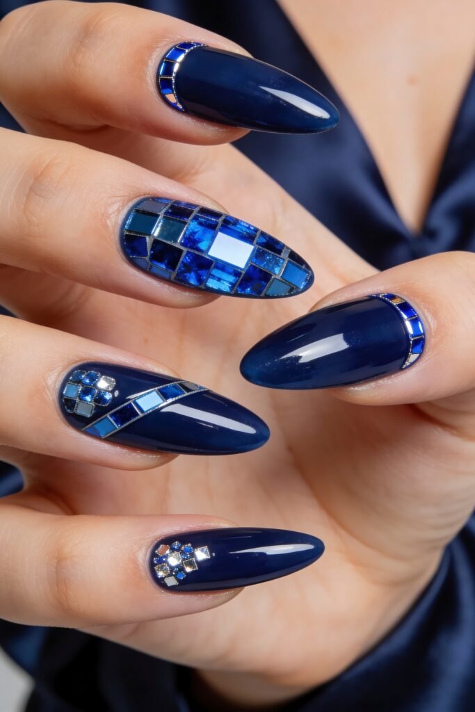 Close-up of deep navy almond nails with blue mosaic tile accents, geometric crystal clusters, and metallic outlines
