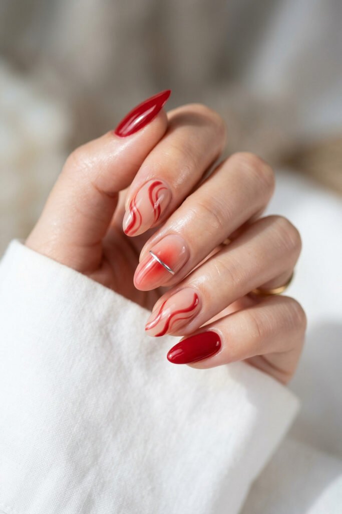 Close up of almond nails with red swirl nail art a soft red ombre accent with silver stripe and glossy red polish