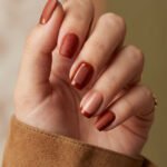 Black and Red Nails for a Bold, Polished Look Soft square fall red nails in terracotta and brown tones with matte speckles, glossy amber jelly, a nude French tip, and dotted accent details.