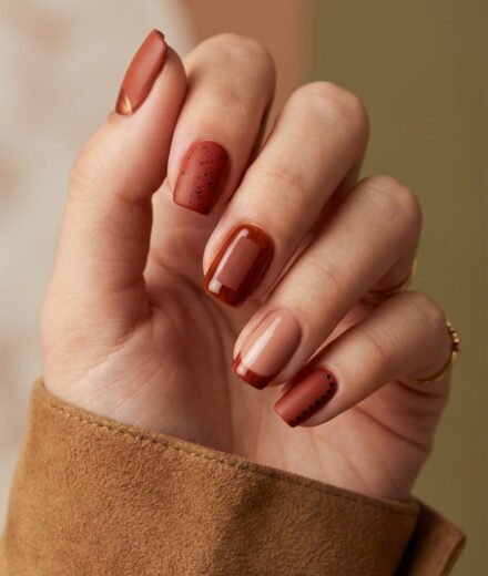 Soft square fall red nails in terracotta and brown tones with matte speckles, glossy amber jelly, a nude French tip, and dotted accent details.