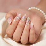 Spring Summer Nails That Feel Fresh and Easy Glossy almond floral spring nails with sheer milky nude base, pressed pink, blue, and white flowers, and subtle gold foil on a soft satin background.